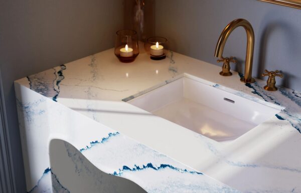Close-up view of installed bathroom countertops using Cambria Inverness Bristol Bay Quartz countertop featuring stormy-blue waves, cool white backdrop, and debossed Inverness veins, showcasing its high gloss finish and durability for residential and commercial applications.